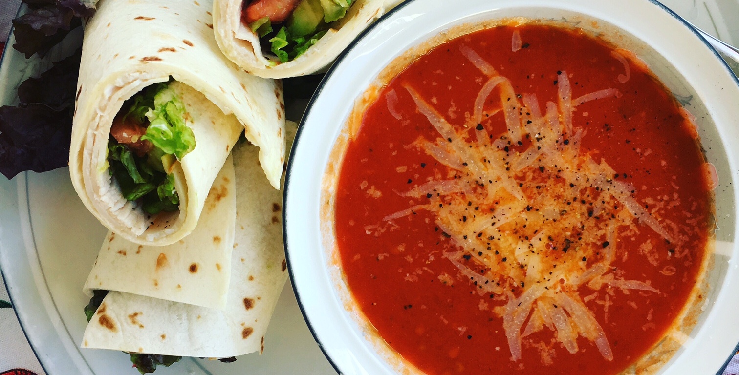 A bowl of tomato soup with a wrap next to it.