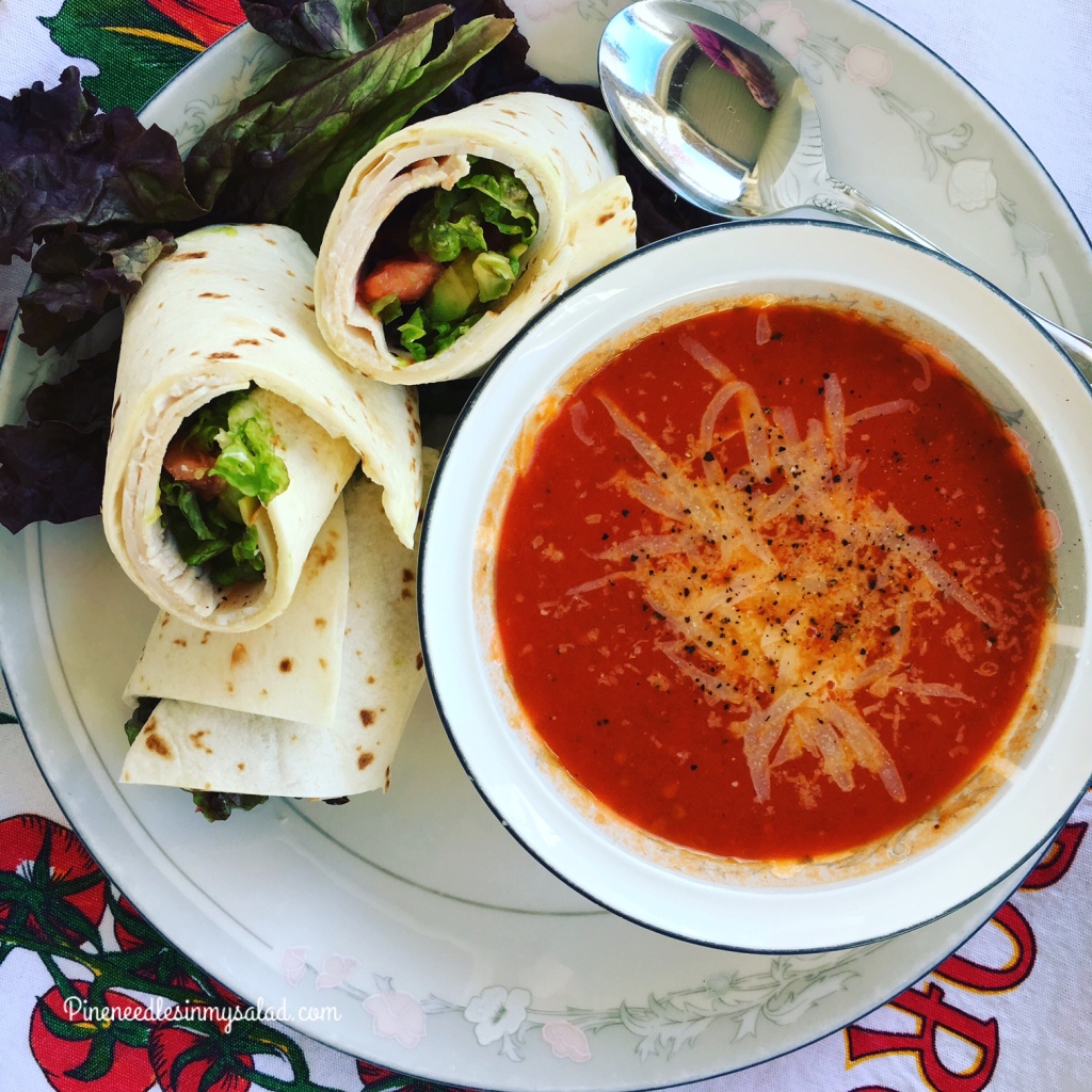 A bowl of tomato soup with a wrap next to it.